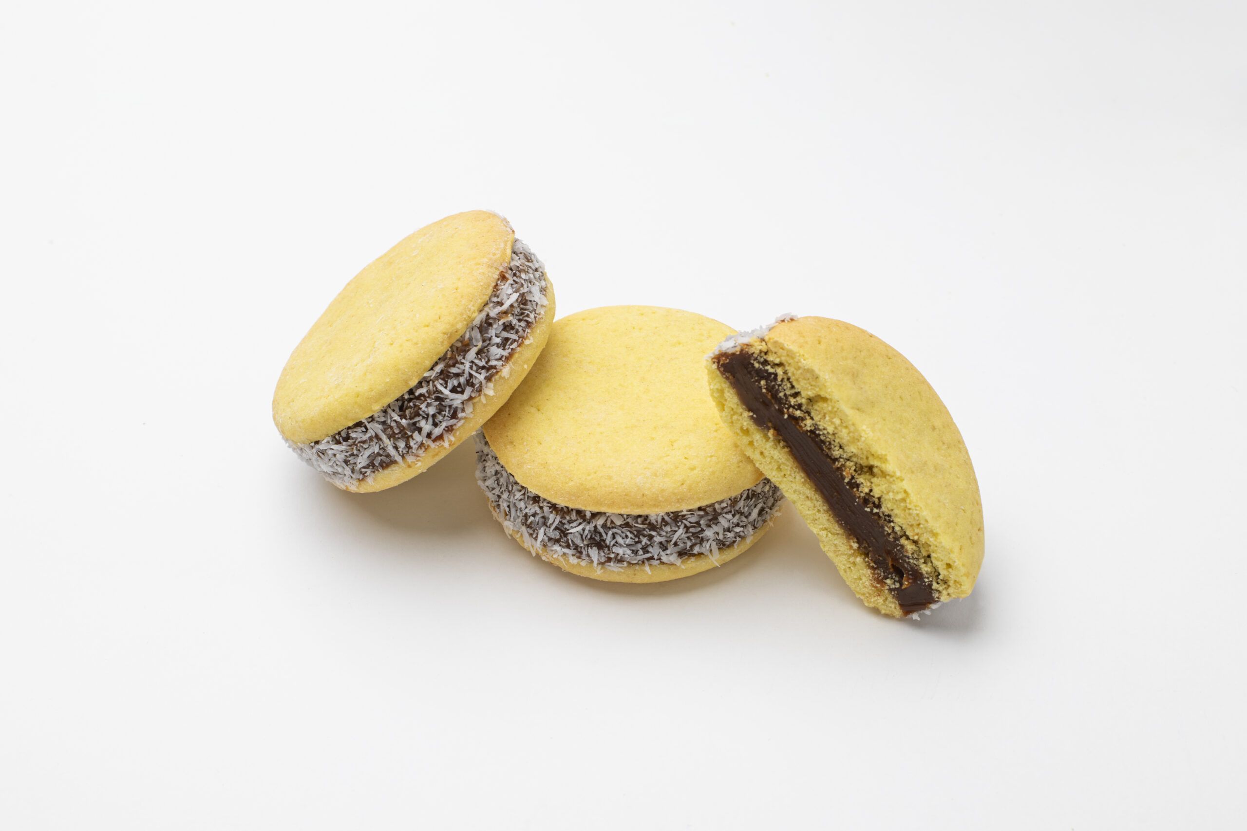 Foto de 3 alfajores de maicena de Argenpastry SL: 2 enteros y uno partido a la mitad para mostrar el relleno de dulce de leche y coco